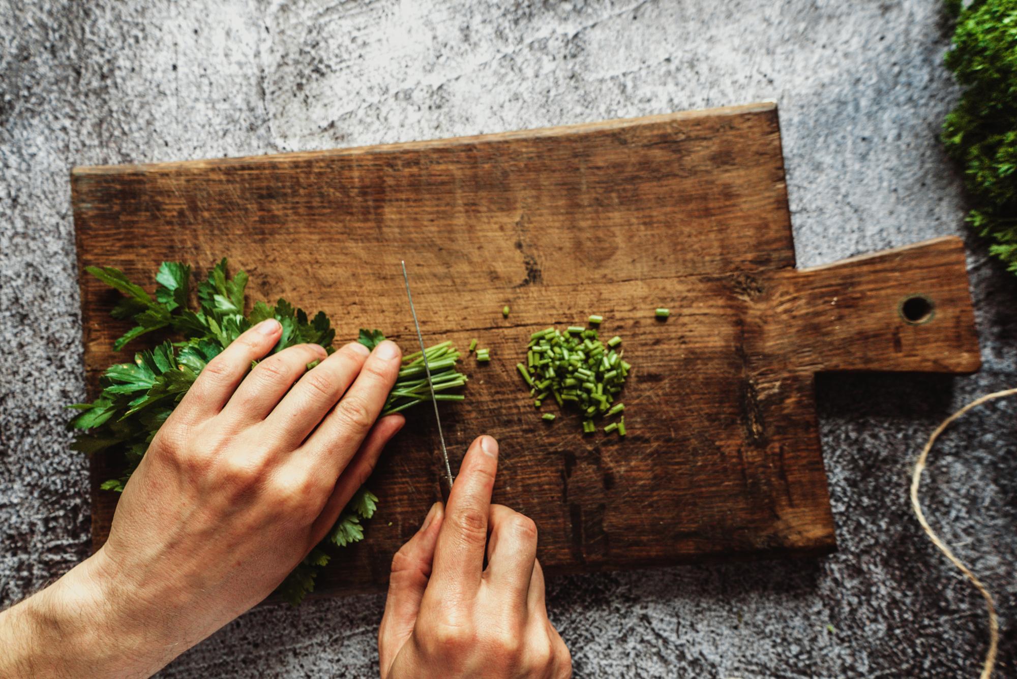 Close-up of chef's hands slicing herbs on wooden board